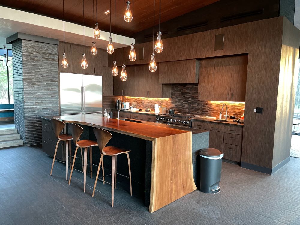 Waterfall live edge solid wood slab kitchen island extension with designer lighting and stools.