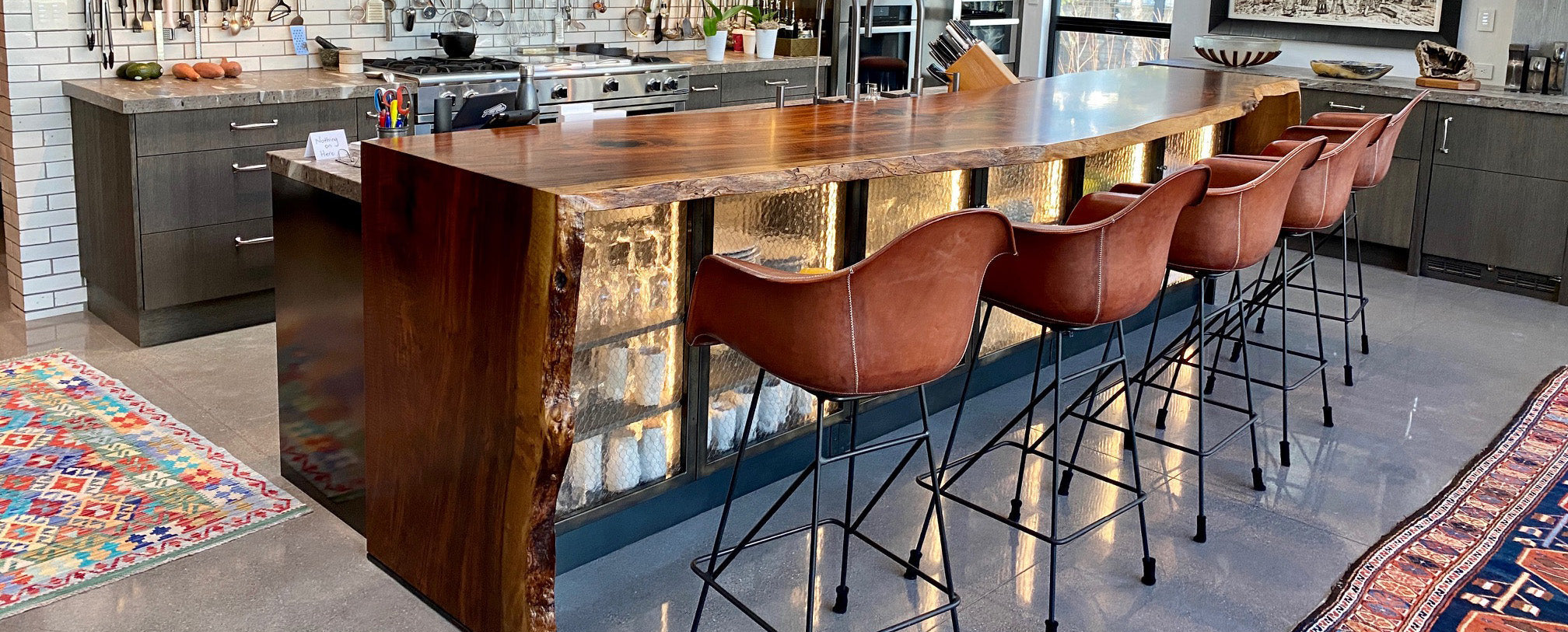 Luxury kitchen design with waterfall style live edge Claro walnut kitchen island extension and leather bar seats. 